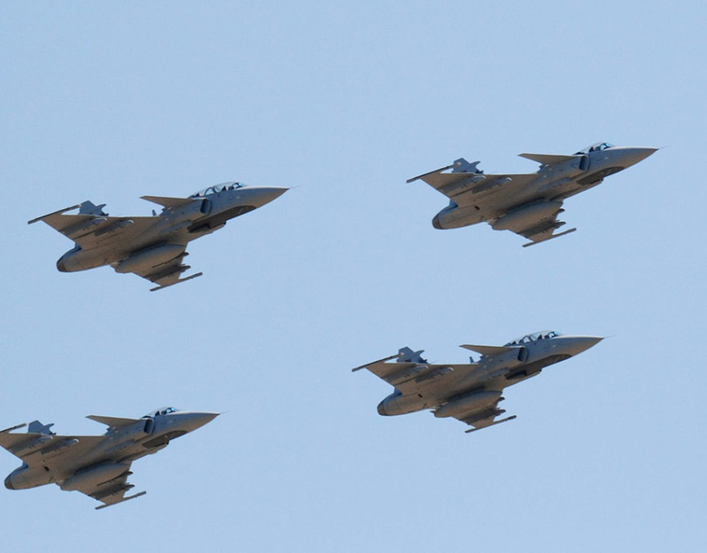Four fighter jets are flying in formation against a clear blue sky.